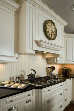 a clock mounted on the wall above a stove in a kitchen with white cabinets and black counter tops