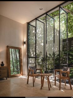 two wooden chairs sitting next to each other in front of a glass wall with trees