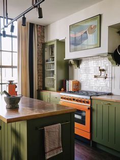 a kitchen with green cabinets and an orange stove top oven next to a large window