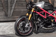 a red and black motorcycle parked in front of a wooden building with it's exhaust pipe out