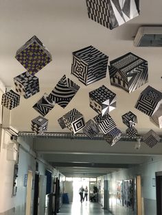 several black and white cubes are hanging from the ceiling in an empty hallway with people walking by