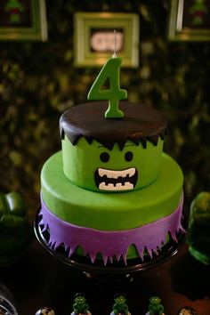 a green and purple cake sitting on top of a table next to cupcakes