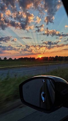 the sun is setting behind clouds in the sky as seen from a car's side view mirror