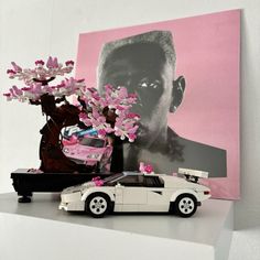 a toy car is parked next to a pink flowered tree on top of a shelf