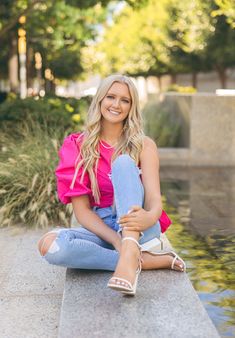 a woman sitting on the edge of a pond with her legs crossed and smiling at the camera