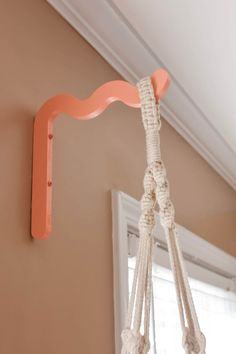 a rope hanging from the ceiling in front of a window with an orange hook on it