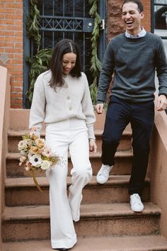 a man and woman holding hands walking down some steps together with flowers in their hand