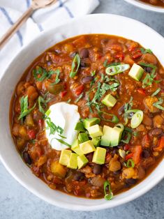 a white bowl filled with chili, avocado and sour cream sitting on top of a table