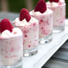 small desserts with raspberries and whipped cream in them on a white tray