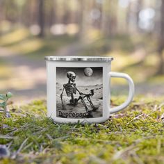 a white coffee mug sitting on top of a grass covered field next to a small plant