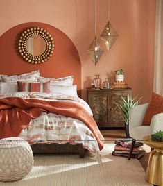 a bedroom with an orange wall and white bedding, gold mirror on the wall