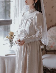 a woman wearing a white dress and veil standing in front of a table with flowers