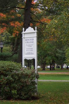 a white sign sitting in the middle of a lush green park next to a tree