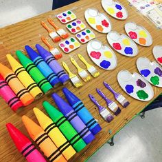 the table is covered with many different colored paints and crayons on paper plates