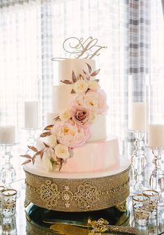 a three tiered cake with flowers on the top is surrounded by candles and glassware