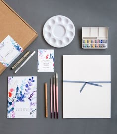 the contents of a stationery set laid out on top of a gray surface with paint and paper