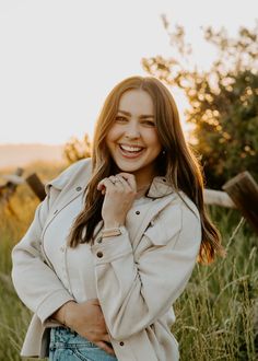 a woman standing in tall grass with her hands on her chest and smiling at the camera