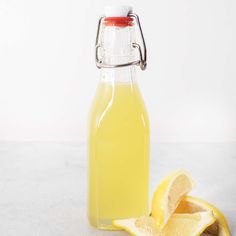 a glass bottle filled with lemonade next to a sliced lemon on a white surface