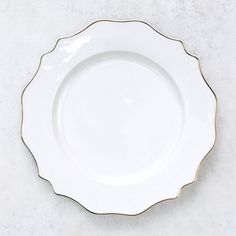 an empty white plate with gold trim on a marble countertop, viewed from above