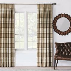 a chair and window in a room with plaid curtains on the windowsill, and a round mirror hanging above it