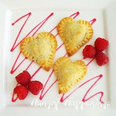 three heart shaped pastries on a white plate with raspberries and drizzled