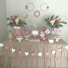 a table topped with lots of pink and white desserts next to vases filled with flowers