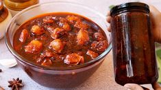 a person holding a jar of chili next to some spices and an empty glass container