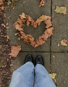 a person standing in front of a heart made out of leaves on the ground with their legs crossed