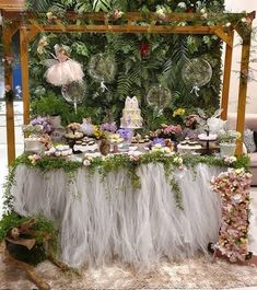 a table topped with lots of cake and desserts next to a lush green wall