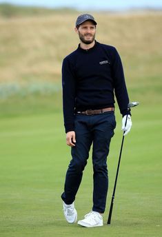 a man standing on top of a green field holding a golf club and wearing a hat