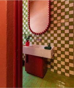 a bathroom with green and white checkered walls, a red vase on the sink