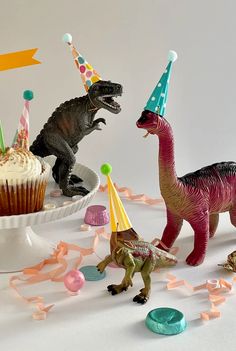 two toy dinosaurs with party hats and cupcakes