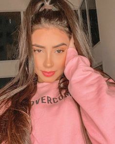 a woman with long hair wearing a pink sweatshirt and holding her hand on her head