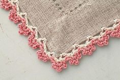 a piece of cloth with pink and white crochet on the edge, laying on a table