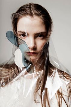 a woman with long hair wearing a clear plastic cover over her face and neck, looking at the camera