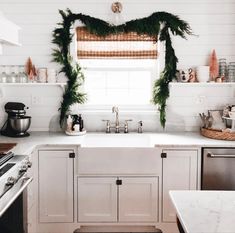 a kitchen decorated for christmas with greenery on the window sill and white cabinets