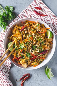 a white bowl filled with noodles and vegetables on top of a red napkin next to chopsticks