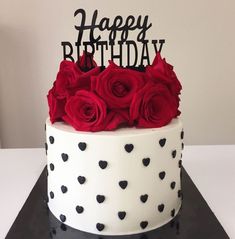 a white and black cake with red roses on the top is decorated with happy birthday lettering