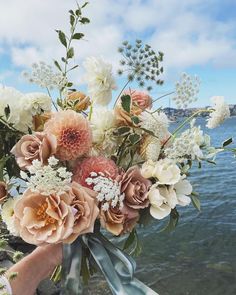 a bouquet of flowers is being held up by someone's hand near the water