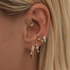 a woman wearing three different types of ear piercings on her left ear and the other one is gold