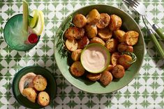 a green bowl filled with potatoes next to two small bowls full of dipping sauces