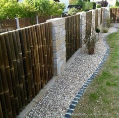 a wooden fence next to a grassy area with rocks and gravel on the ground in front of it