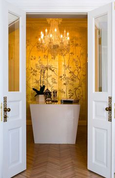 an open door leading to a bathroom with a tub and chandelier