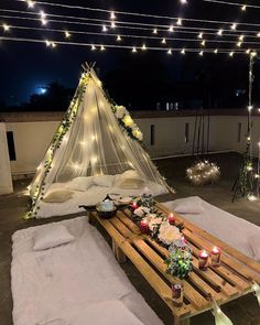 a table with candles and flowers on it in front of a teepee at night