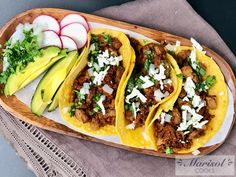 three tacos with meat, cheese and avocado on a wooden platter