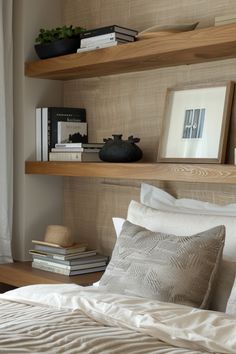 Cozy bedroom with wooden shelves displaying books, decor items, and a framed picture above a neatly made bed with neutral-toned bedding. Behind Bed Shelves, Shelf Over Dresser, Shelves Next To Bed, Decorating Shelves In Bedroom, Bedroom Shelves Ideas, Curated Shelves, Bedroom Shelf Ideas, Bedroom Shelving Ideas, Shelf Over Bed