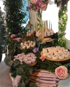 a table topped with lots of cupcakes covered in pink frosting and greenery