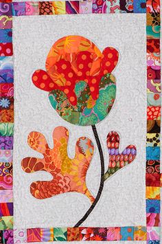 a patchwork quilt with an orange flower on the center and two hands in the middle