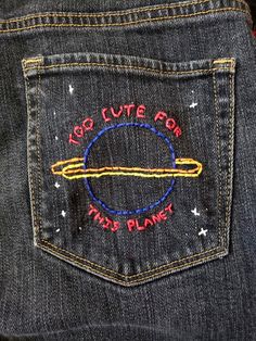 the back pocket of a pair of jeans with an embroidered space shuttle patch on it