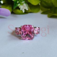 three stone ring with pink stones on white surface next to green leaves and purple flowers